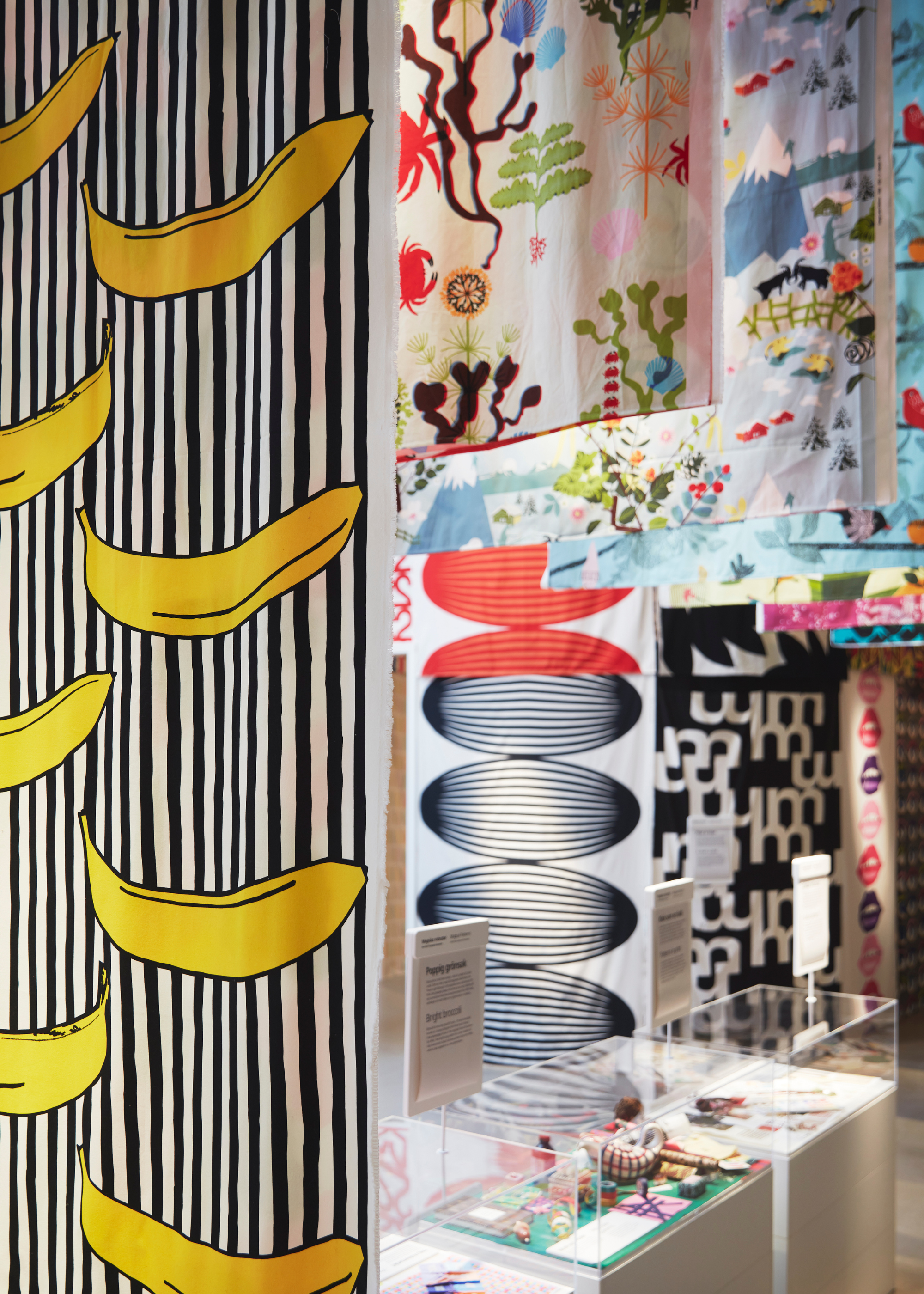 A black and white striped textile with animated banana illustrations is at the front of a row of colorful patterned fabrics over display cases