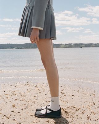 a model on a beach wearing a sandy liang mini skirt and sandy liang mary jane snekears