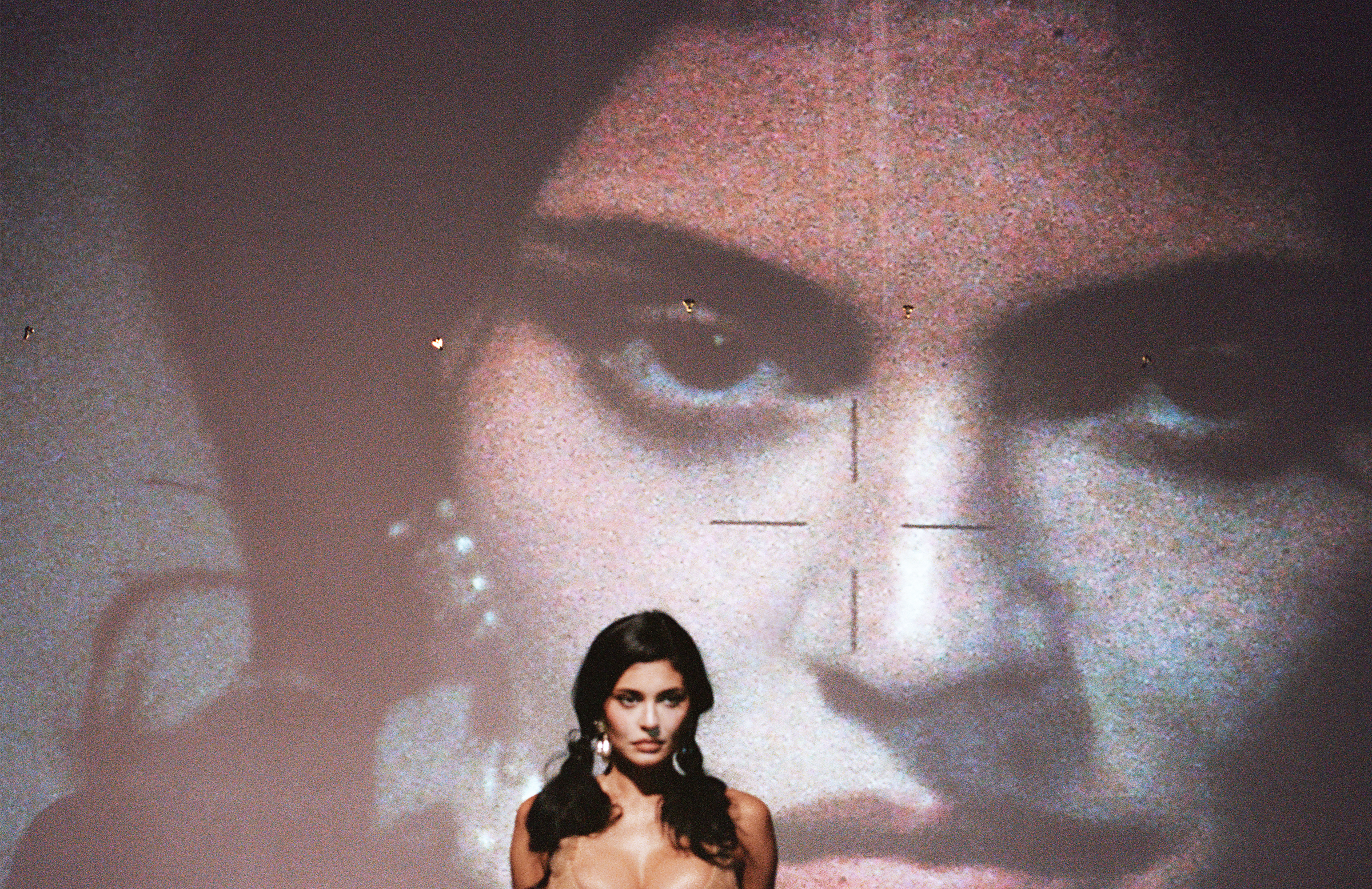 Kylie Jenner standing in front of a wall where her image is projected behind her.