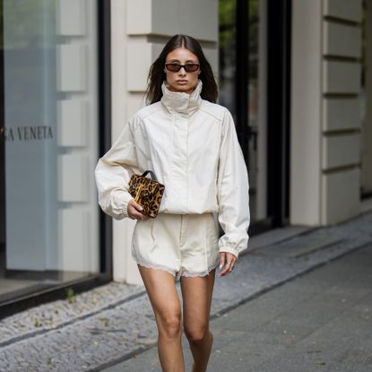 stylish woman wearing a cream funnel neck jacket and cream silk shorts