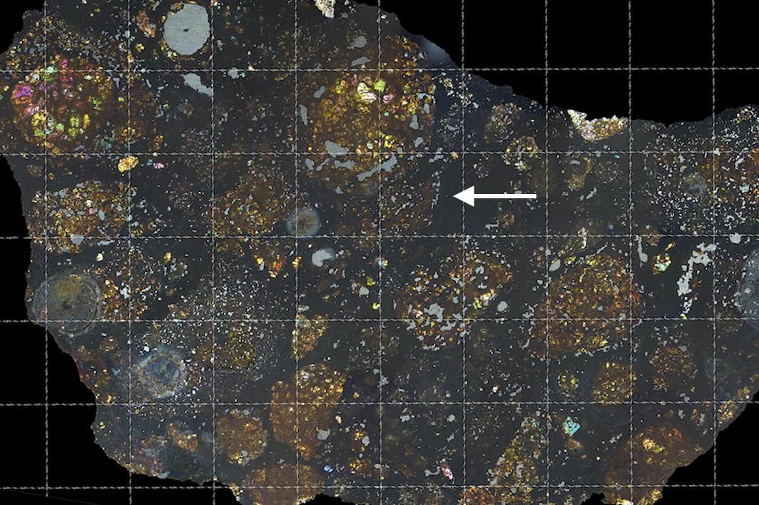 Scientists found the carbon-rich fragment of a comet embedded within a meteorite (at white arrow). The meteorite&#039;s colors can be seen by shining polarized light through a thin slice, and the grid lines show intervals of one millimeter.