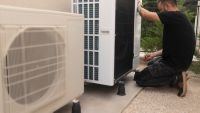 A man installing a heat pump next to another one
