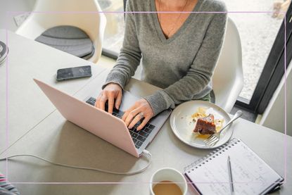 A faceless woman typing on a laptop at a kitchen table