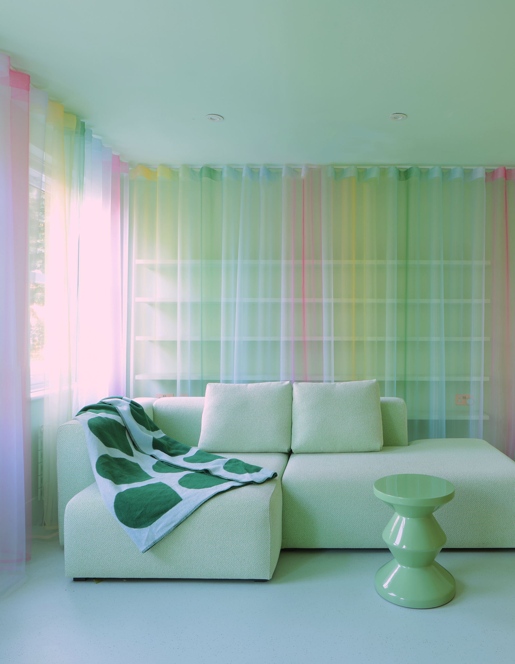 A mint green coloured living room with a modern style sofa and multi coloured mesh curtains surrounding the space.