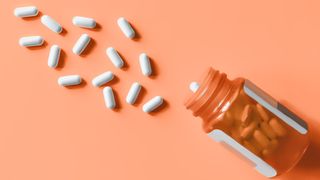 bottle of pills spilling out on orange background