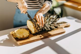 A woman slicing pineapple on a chopping board