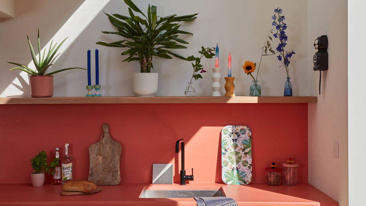 Orange kitchen counter and backsplash decorated with plants, candlesticks and kitchenware.