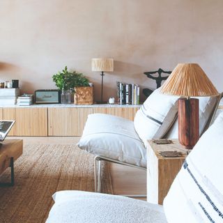 A living room with limewash-effect walls and a low storage unit with a tiled top and reeded doors