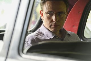 Gary Baines (Alexander Cobb) sits in the back of a car, giving a side-glance out of the window. He looks a little bit suspicious.