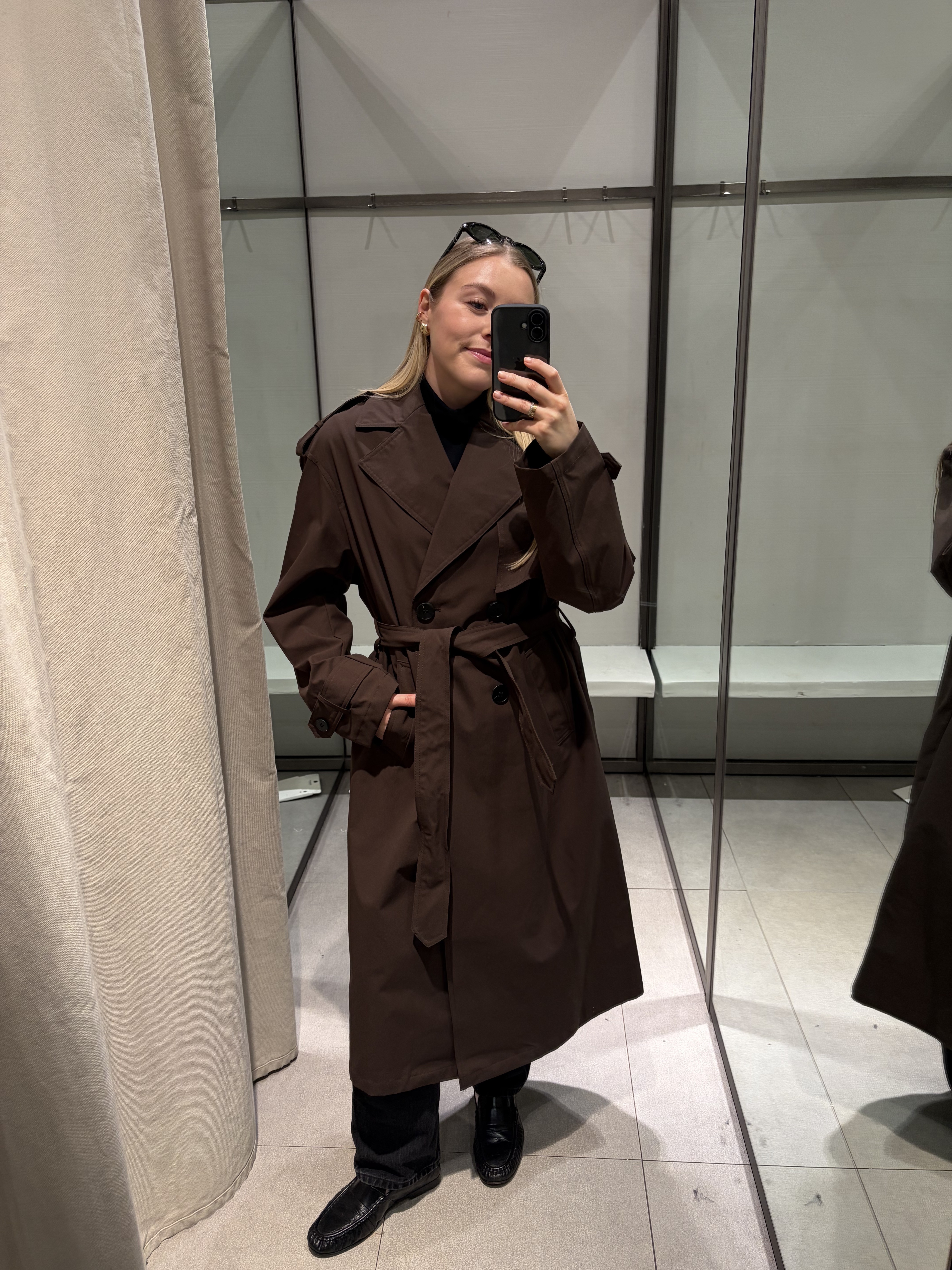 Woman wears brown trench coat, black jeans and black loafers