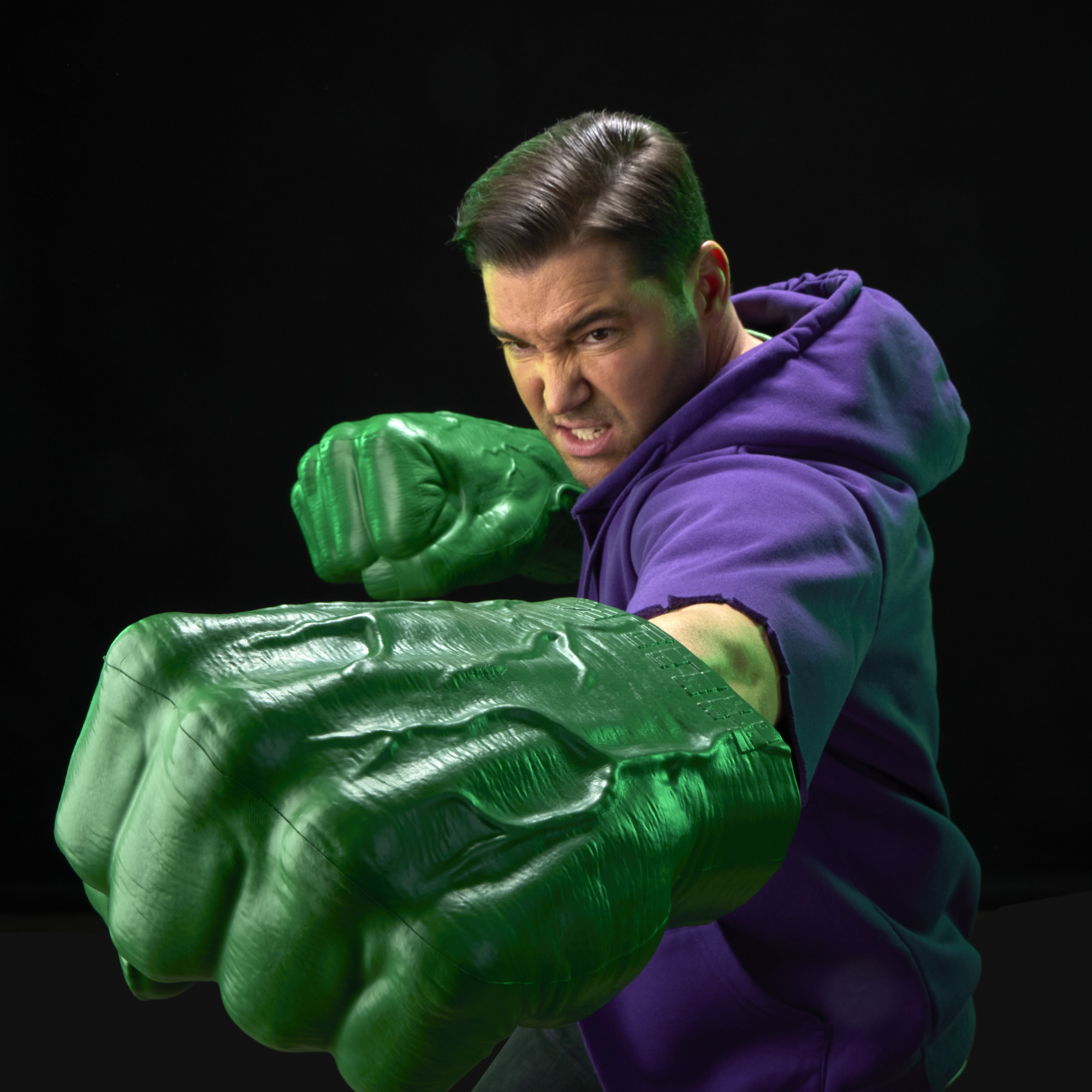 A roaring man with two Hulk Fists pretends to punch with them against a black background