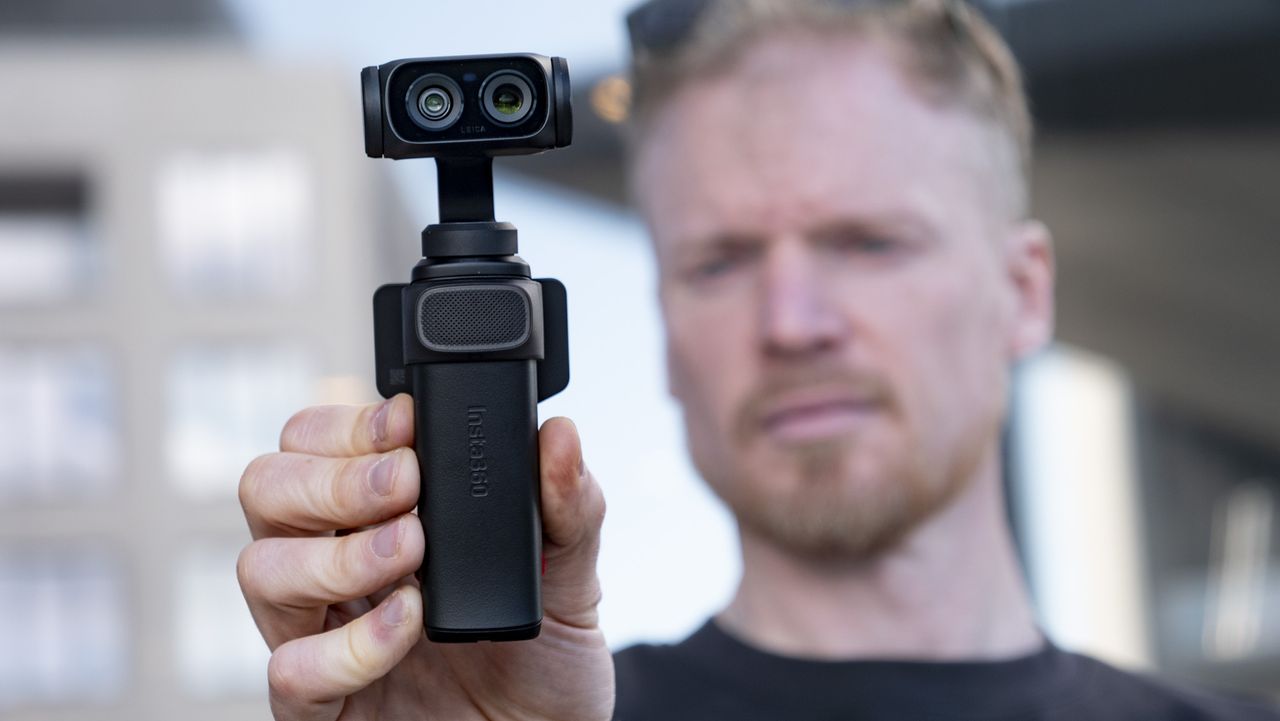 Man holding the Insta360 Luna Ultra vlogging camera, outdoors in a gray urban scene