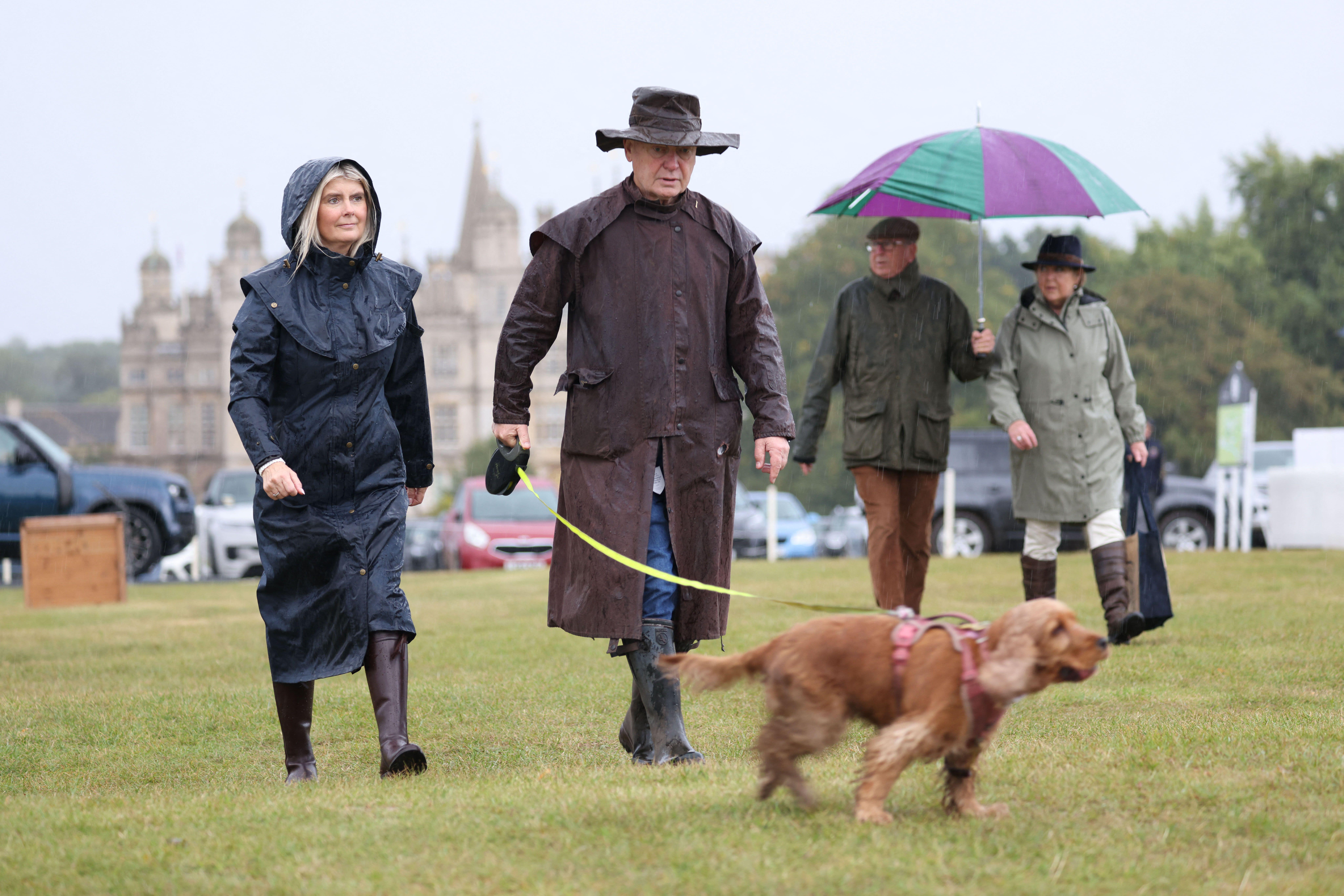 Couple with a dog walking in front of Burghley House, dressed in long waterproof coats