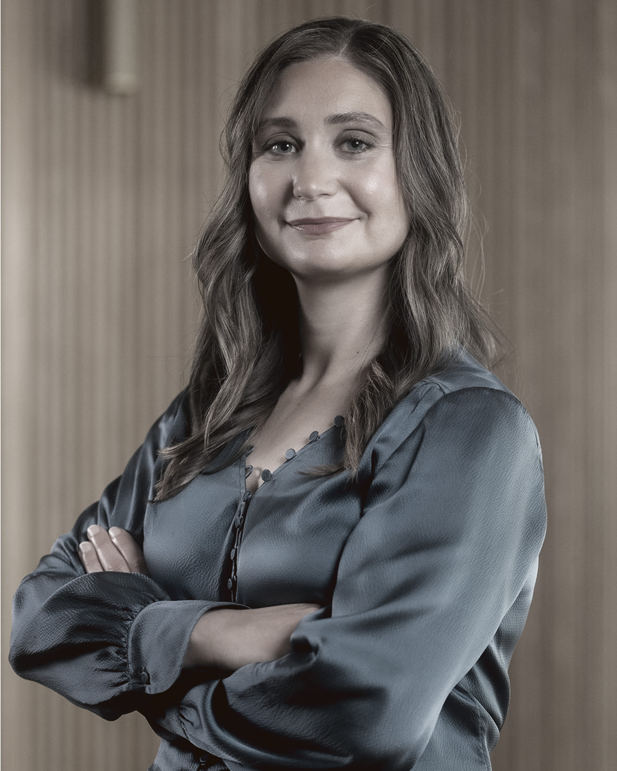 Daniela Amodei standing with arms crossed, smiling in a silky blouse with a neutral background.