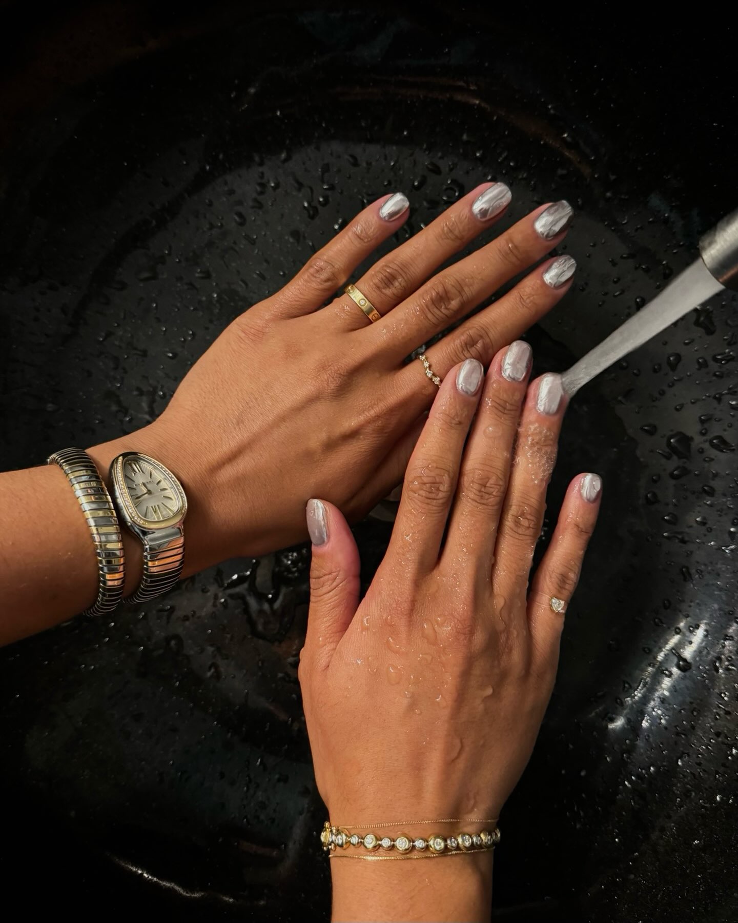 Silver chrome manicure on short nails, hands wearing rings and a wrap watch