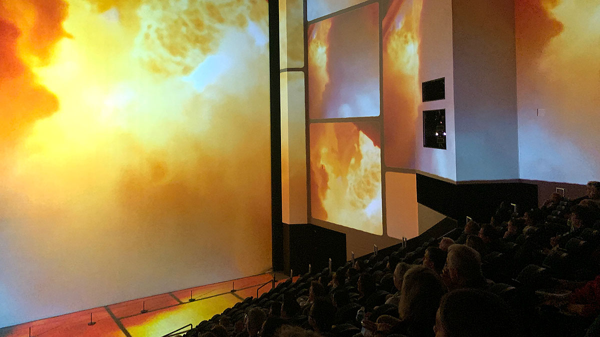 footage from the launch of a rocket is projected onto a giant movie screen as well as the theater's walls and floor