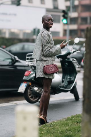 A guest at Milan Fashion Week Fall 2025 in street style in a gray skirt suit and red Gucci bag