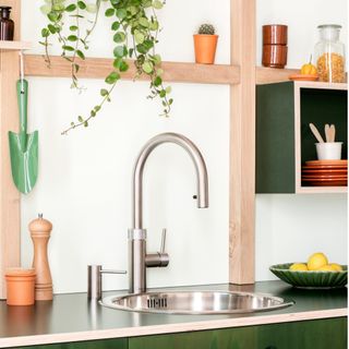 boiling water tap on a green worktop with a bowl of lemons a wooden pepper grinder and a green spade