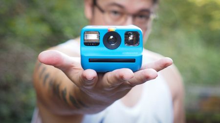 Photographer James Artaius holding a Blue Polaroid Go Gen 2 camera, in a woodland setting