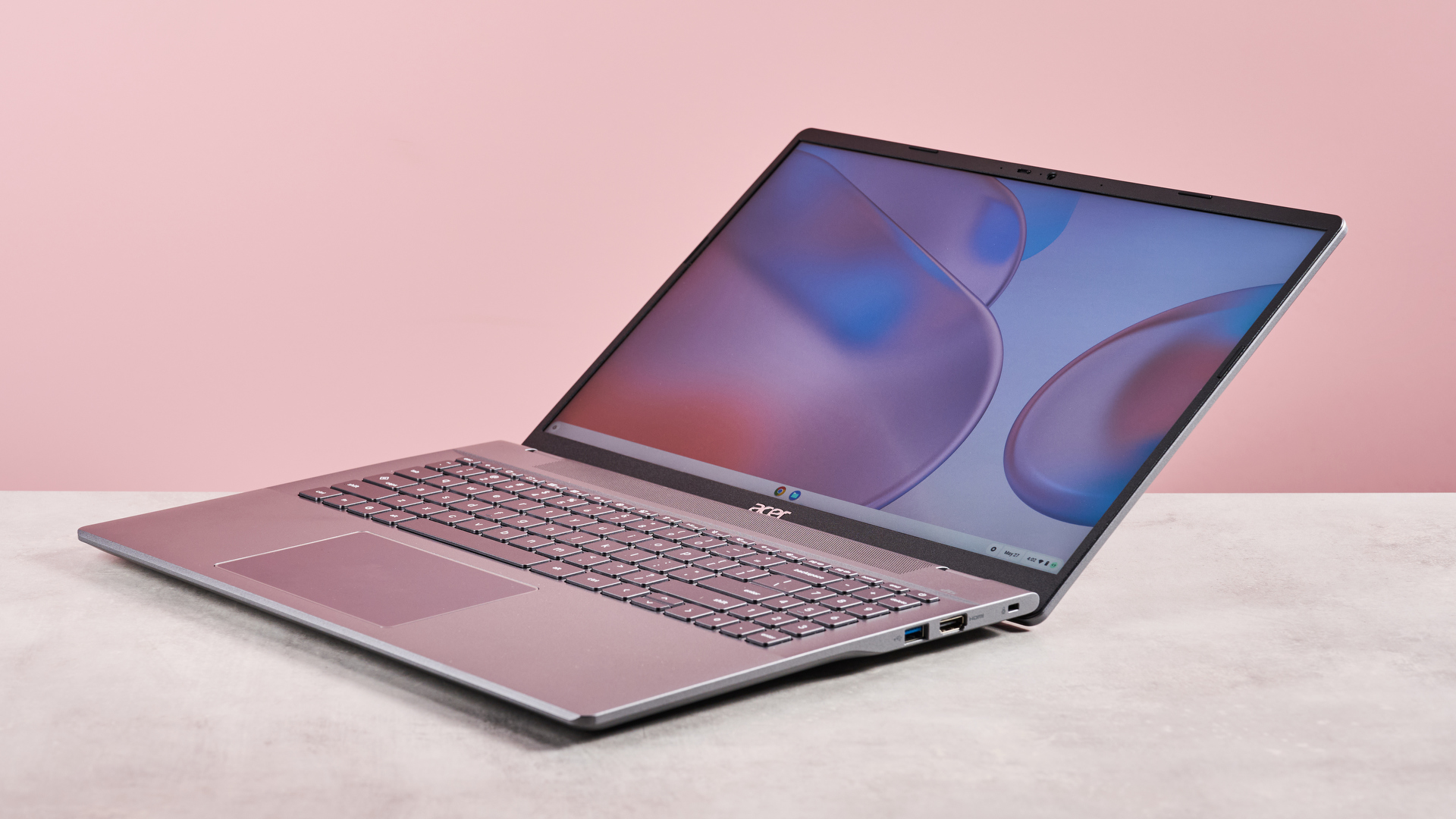 Three-quarter view of Acer Chromebook Plus 514 open wide on desk with pink background