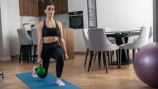 Woman exercising at home with kettlebell. She is in a lunge position.