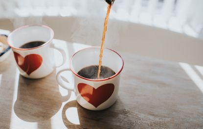 Pouring black coffee into coffee cups with heart design Space for copy Conceptual