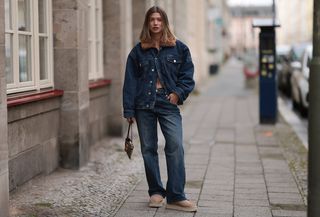 Sophia Geiss is seen wearing various-sized golden hoop earrings, an oversized dark blue denim jacket with a brown faux fur collar from Worst Behavior, matching straight-legged jeans with orange decorative seams also from Worst Behavior, a rectangular brown logo-patterned vintage handbag from Fendi, oval rimless black sunglasses from Vehla Eyewear in her hand, and sand-colored platform shoes from Ugg on September 26, 2024 in Berlin, Germany. (Photo by Jeremy Moeller/Getty Images)