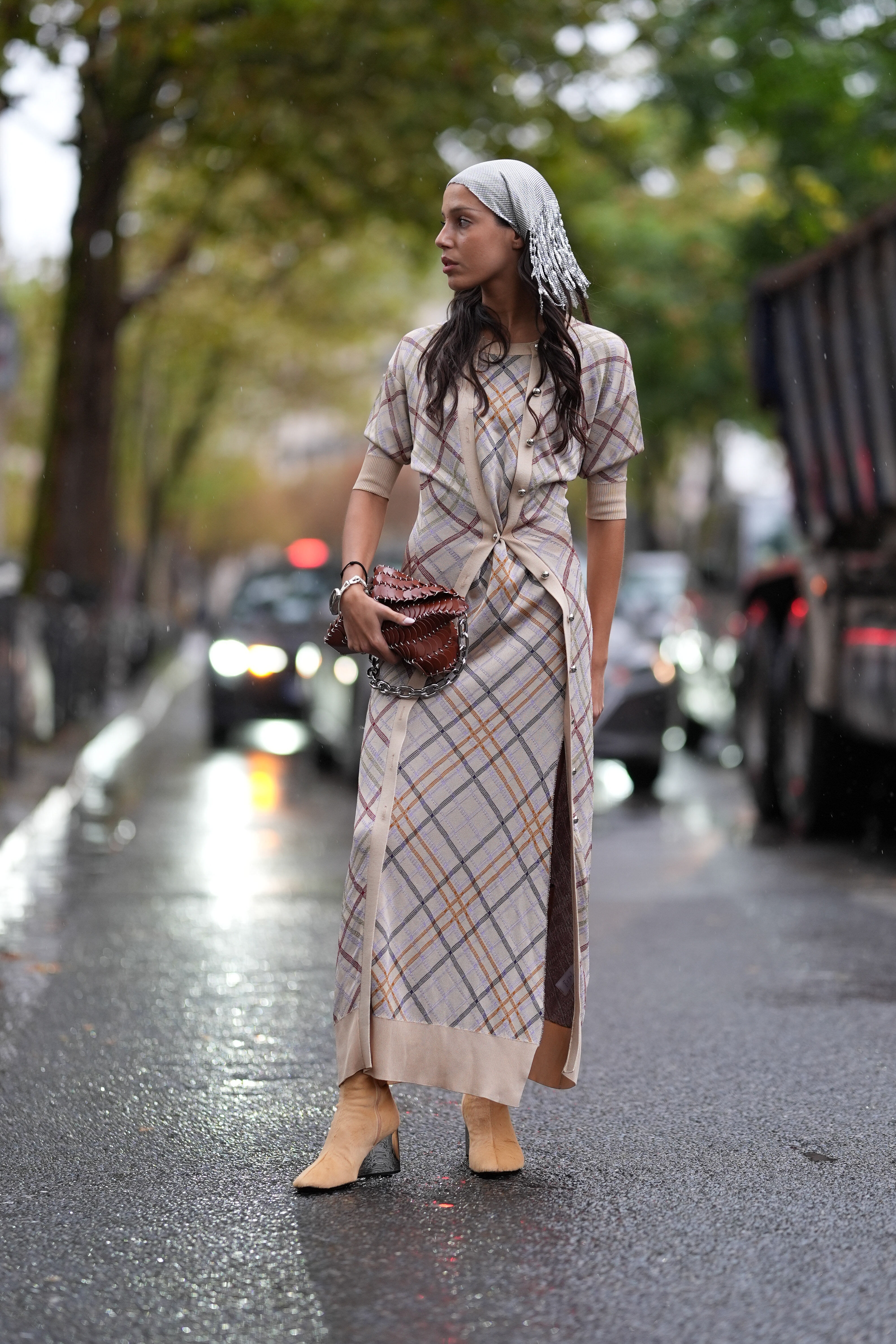 Una invitada lleva una diadema blanca, un vestido largo a cuadros beige, un bolso Rabanne con cadena marrón y tacones de ante beige, en la puerta de Rabanne, durante la Semana de la Moda de París Primavera/Verano 2025 para mujer.