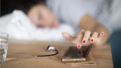 Woman in bed reaches over to tap ringing smartphone for morning wakeup call.