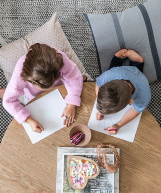 Two children draw at a home art station on a wooden table