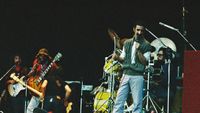 Frank Zappa performs on stage with band members (L-R) Denny Walley, Ike Willis, Arthur Barrow (back to camera) and drummer Vinnie Colaiuta at The Knebworth Festival on September 9th, 1978 