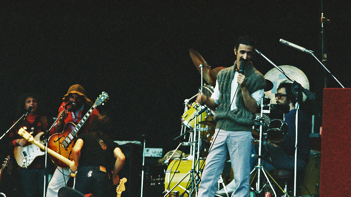 Frank Zappa performs on stage with band members (L-R) Denny Walley, Ike Willis, Arthur Barrow (back to camera) and drummer Vinnie Colaiuta at The Knebworth Festival on September 9th, 1978 