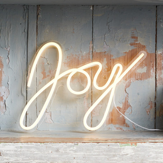 A neon night of the word 'joy' against a light wooden background