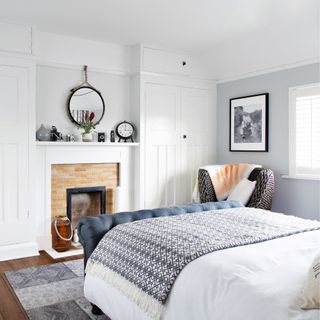 Bedroom with dark wooden floor, built in cupboards either side of the fireplace, pale grey walls and a large double bed with white and black bed covers
