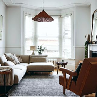 White painted living room with large windows, blinds, L shaped cream sofa