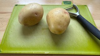 Potatoes and a peeler on a chopping board