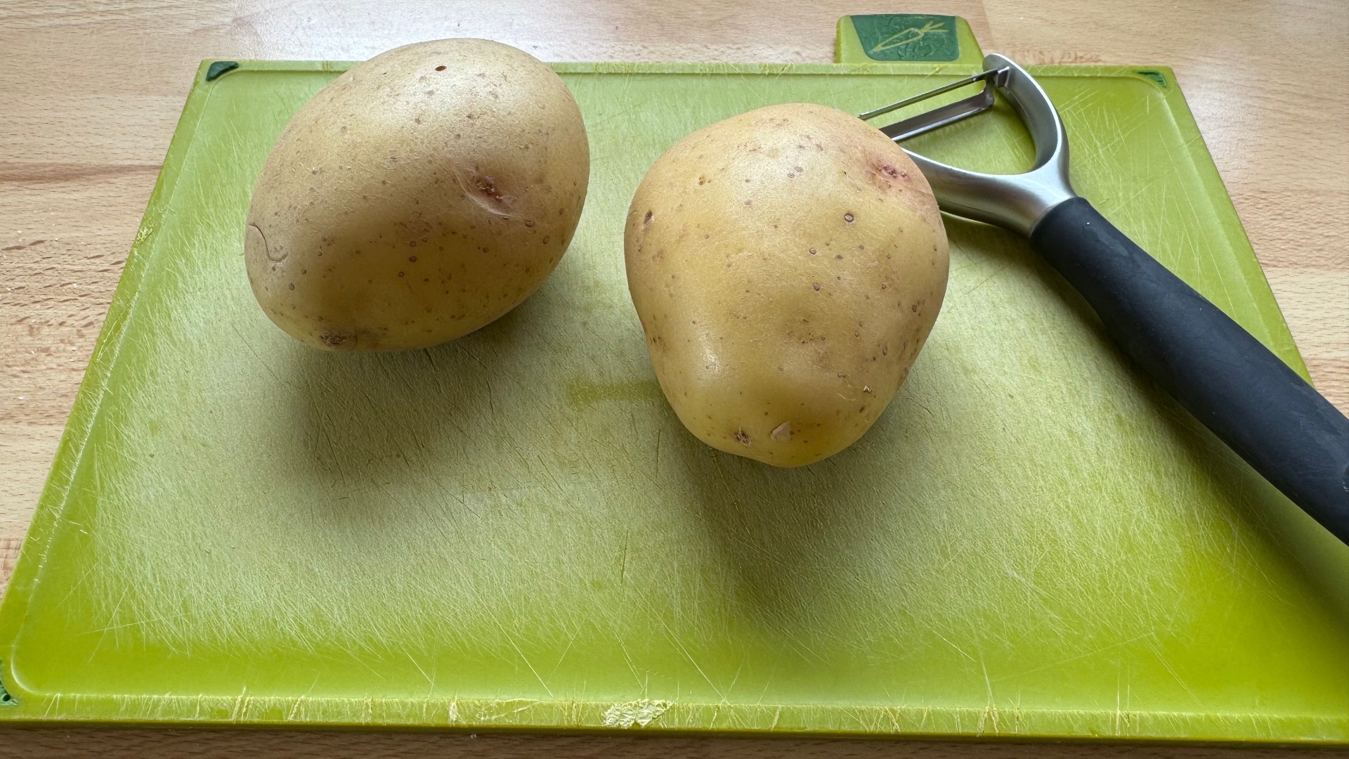 Potatoes and a peeler on a chopping board