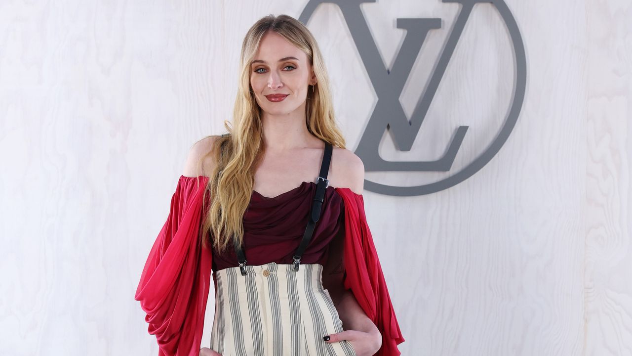 Sophie Turner at Louis Vuitton&#039;s PFW show wearing striped suspender pant with a red draped blousents with a 