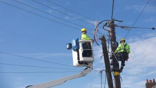Workmen in hi vis jackets checking power supply lines from electrical pole