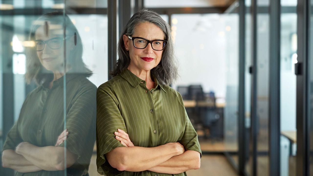 A business executive stands in a corporate office with her arms crossed.