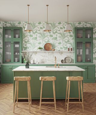 kitchen with herringbone wooden floor, green kitchen island with white worktop, run of green kitchen units and white worktop behind island with green and white wallpaper above, three white and gold pendants above kitchen island, wooden bar stools