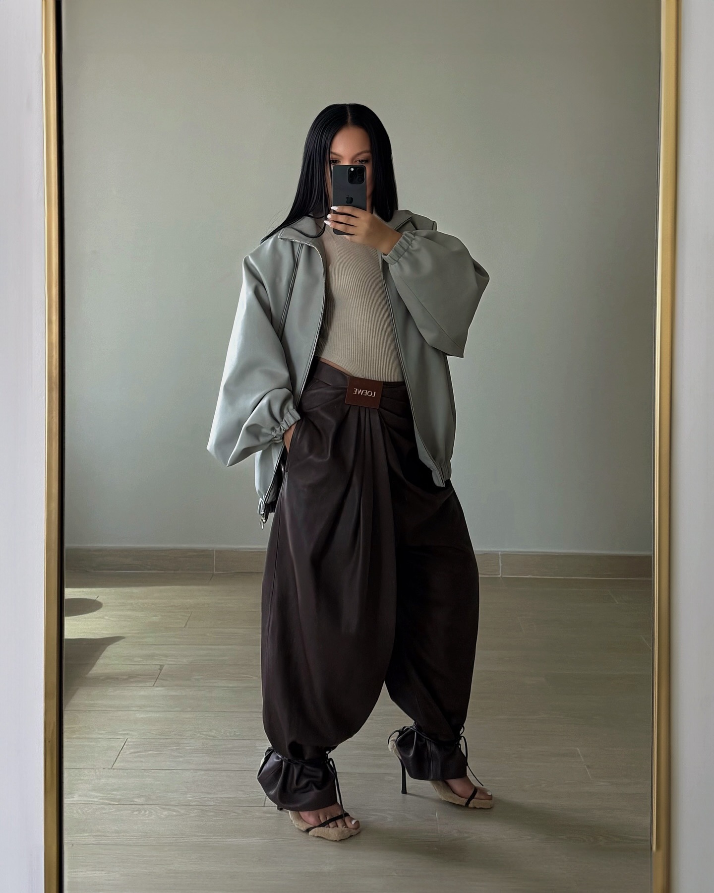 @oumaymaboumeshouli wearing a gray jacket and brown Loewe leather genie pants.