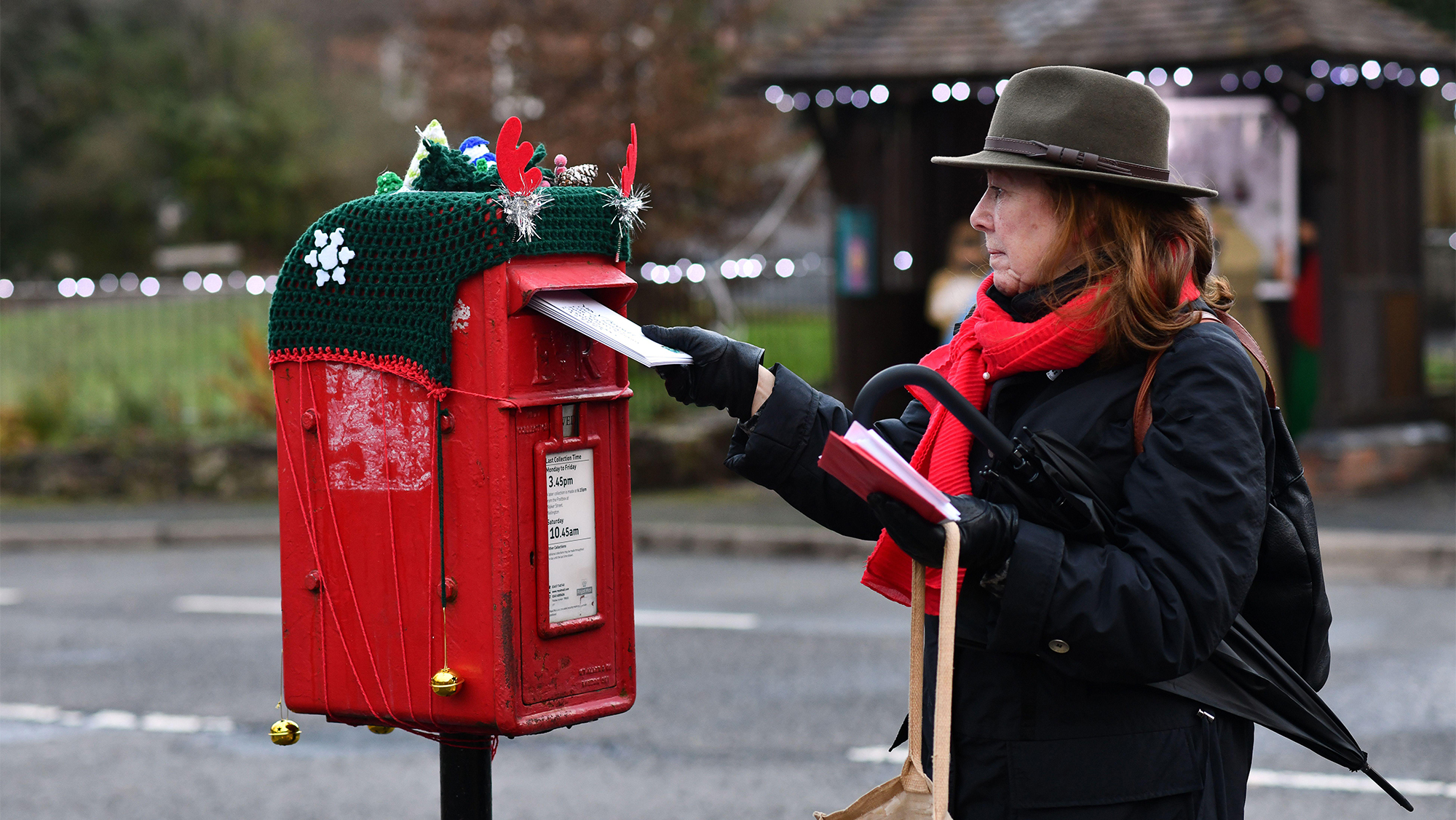 Woman posting Christmas cards in a postbox with knitted Christmas-themed cover