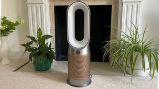 The Dyson Hot + Cool Air Purifier in front of a fireplace with plants around it