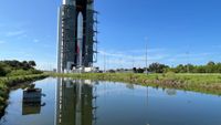 a silver, white and red rocket stands inside a large hangar behind a pond