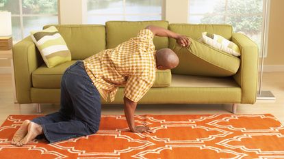picture of man looking for something under a couch cushion