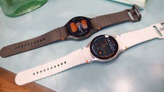 Two models of Samsung Galaxy Watch 7 on a blue table