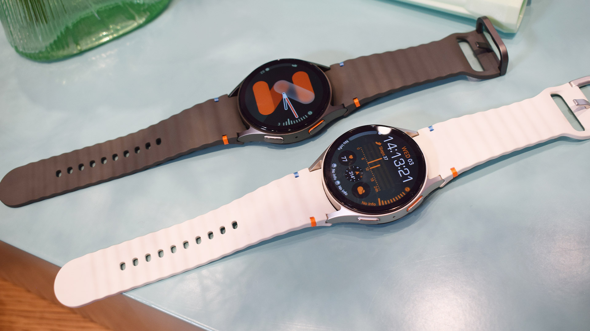 Two models of Samsung Galaxy Watch 7 on a blue table