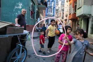 A colorful street scene with children playing and two children centrally framed in a hula hoop