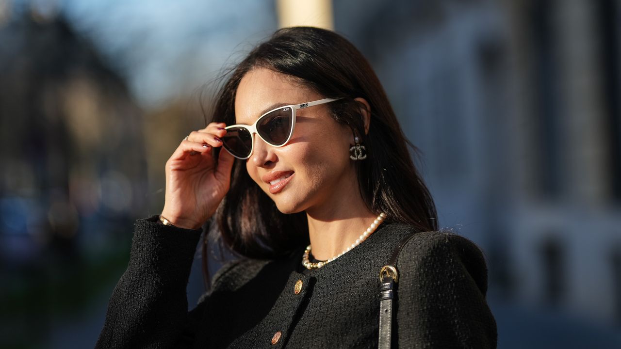 woman wearing sunglasses, black jacket and pearl necklace